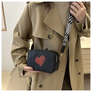 Close-up of black textured leather crossbody bag with red heart and wavy strap