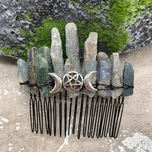 Detail of natural raw crystal hair comb with silver triple moon pentagram on mossy rock