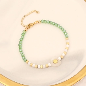 Macro view of heart charm bracelet with light green beads and gold hardware on white plate