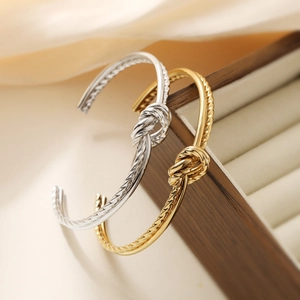 Knot design stainless steel open bangles in gold and silver finish on silk background