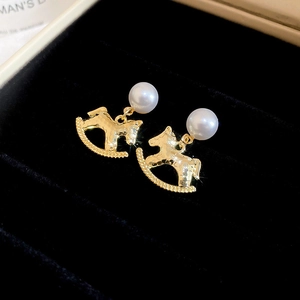 Detailed close-up of golden rocking horse earrings with pearls on black velvet