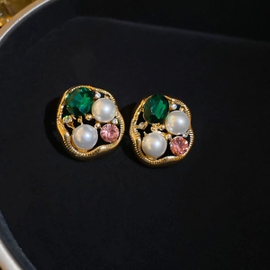 Macro shot of vintage gold earrings with green gems and pearls on black velvet