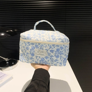 Close-up of a blue floral quilted makeup bag with handle and metal zipper closure