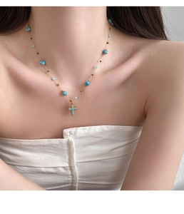 Detail of gold cross necklace with blue beads and stone pendant on a model's neck