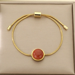 Détail d'un bracelet chaîne serpent dorée ajustable avec une pierre ronde rouge chatoyante