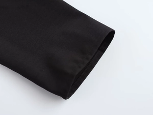 Gros plan des poignets de la robe montrant les coutures fines et le tissu noir de qualité