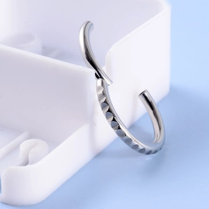 Detailed view of silver stainless steel septum ring with wave texture on a tray