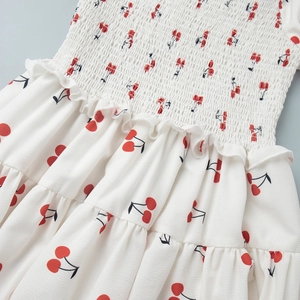 Detail of white dress featuring cherry prints with elastic smocking and ruffle texture