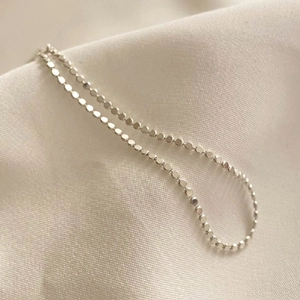Close-up of minimalist S925 sterling silver flat bead anklet on soft beige fabric