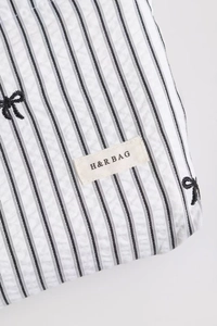 Détail d'une trousse à maquillage rayée avec broderie nœud noir et étiquette H&R BAG