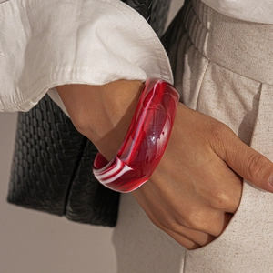 Detail of a wide acrylic resin bangle with red and white marble patterns on a wrist