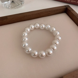 Detailed view of elastic pearl bracelet with white luster on beige fabric background
