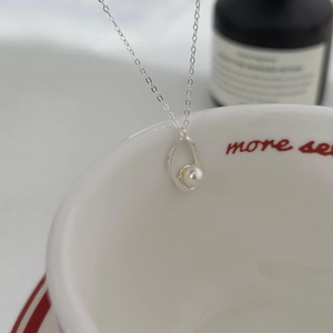 Detail of irregular silver geometric frame holding a white pearl on a fine chain