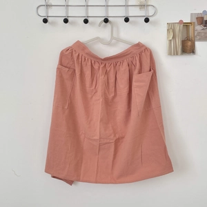 Detail of coral pink cotton apron featuring large utility pockets and pleated waist texture