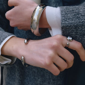 Polished stainless steel bangle and ring set worn over a dark grey wool coat
