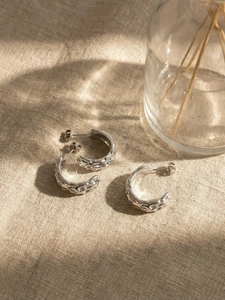 Macro shot of silver C-shaped stainless steel earrings with irregular hammered texture