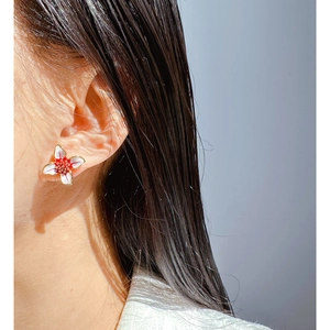 Elegant white enamel flower earrings with red edges worn by a female model