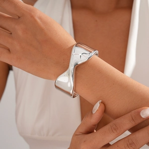 Detailed view of an irregular wide silver metal cuff bracelet with a polished mirror finish