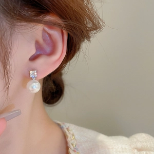 Detailed close-up of an elegant pearl earring with square cubic zirconia studs on ear