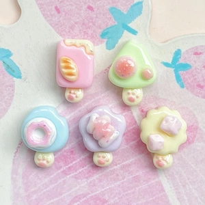 Detail of miniature resin dessert charms featuring cat paw patterns on a pink background