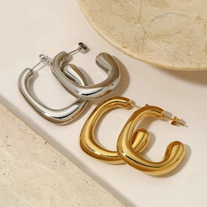 Detail view of thick C-shape gold and silver hoop earrings on a marble surface