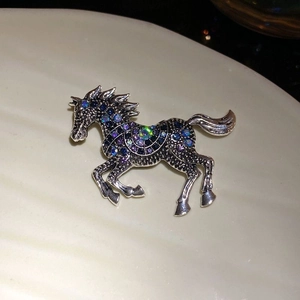 Vintage silver horse brooch with blue and purple rhinestones on a ceramic dish