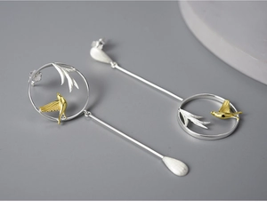 Detailed macro view of S925 silver asymmetric earrings with gold bird and silver leaf motifs