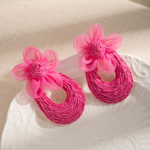 Detail of handmade woven raffia earrings with pink mesh flower petals on ceramic tray