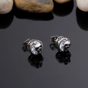 Macro shot of silver skull stud earring with a central zircon on black reflective surface