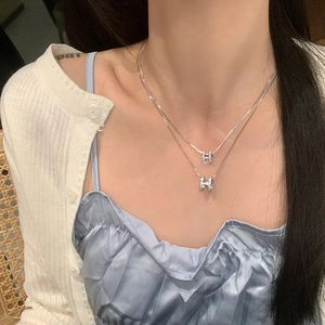 Close-up of layered silver H-letter necklaces with sparkling zircons on female model