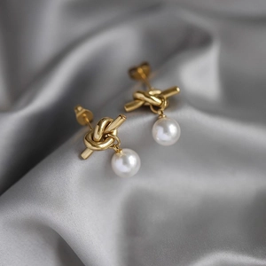 Elegant gold knot stud earrings with round white pearls on grey silk background