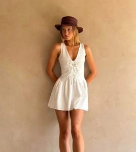 Detail of white V-neck sleeveless dress featuring front lace-up design and ruffled hem
