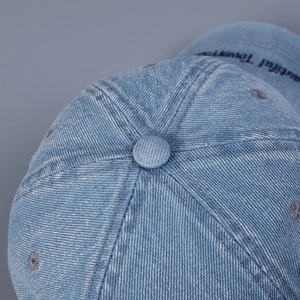 Detail of light blue denim baseball cap showing top button and embroidered eyelets