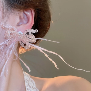 Close-up of pink beaded bow earrings with long feather tassels on a female model