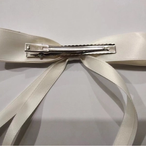 Back view of a white silk bow hair clip showing the silver metal alligator clamp