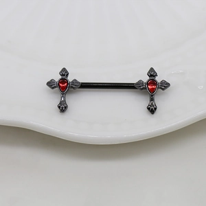 Close-up of black metal cross nipple rings with red gems on a white ceramic plate