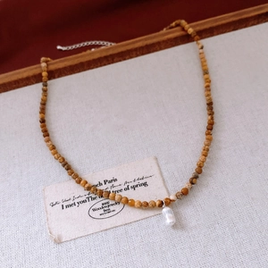 Détail d'un collier de perles avec pendentif perle baroque sur tissu en lin texturé