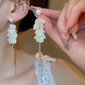 Detail of white petal earrings with golden long chain tassels and faux pearl studs