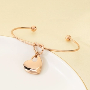 Detailed shot of rose gold knotted cuff bracelet with a polished heart pendant charm
