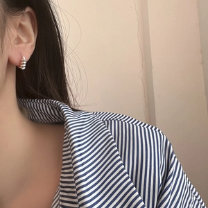 Détail de boucles d'oreilles créoles torsadées argentées au design minimaliste sur l'oreille