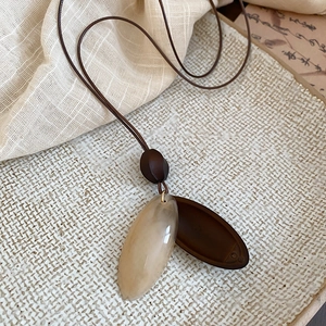 Detailed view of the oval resin and wood pendant on a brown cord with a textured backdrop