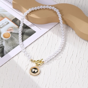 Detail view of pearl necklace with gold OT clasp and black bow pendant on white backdrop