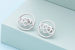 Detailed view of silver heart and infinity symbol stud earrings on a blue geometric stand