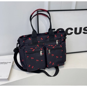 Detail of black nylon tote with red cherry print featuring multi-zippered front pockets