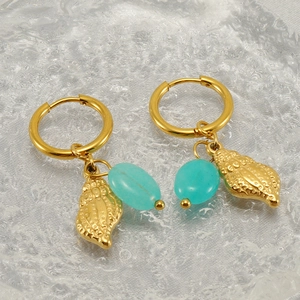 Detail of golden hoop earrings featuring turquoise beads and shell charms on glass