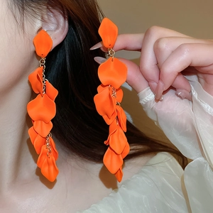 Detail showing long orange petal tassel earrings with a matte finish worn by a model