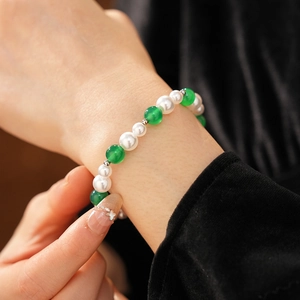 Primo piano di un bracciale vintage con agate verdi e perle bianche su un polso