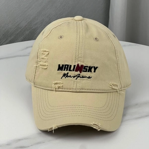 Close-up of beige baseball cap featuring distressed holes and MALINSKY embroidery details