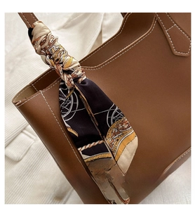 Gros plan sur l'anse d'un cabas en cuir marron avec un foulard en soie au motif de chaîne