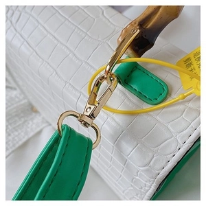 Close-up of white crocodile pattern bag with bamboo handle and green strap detail